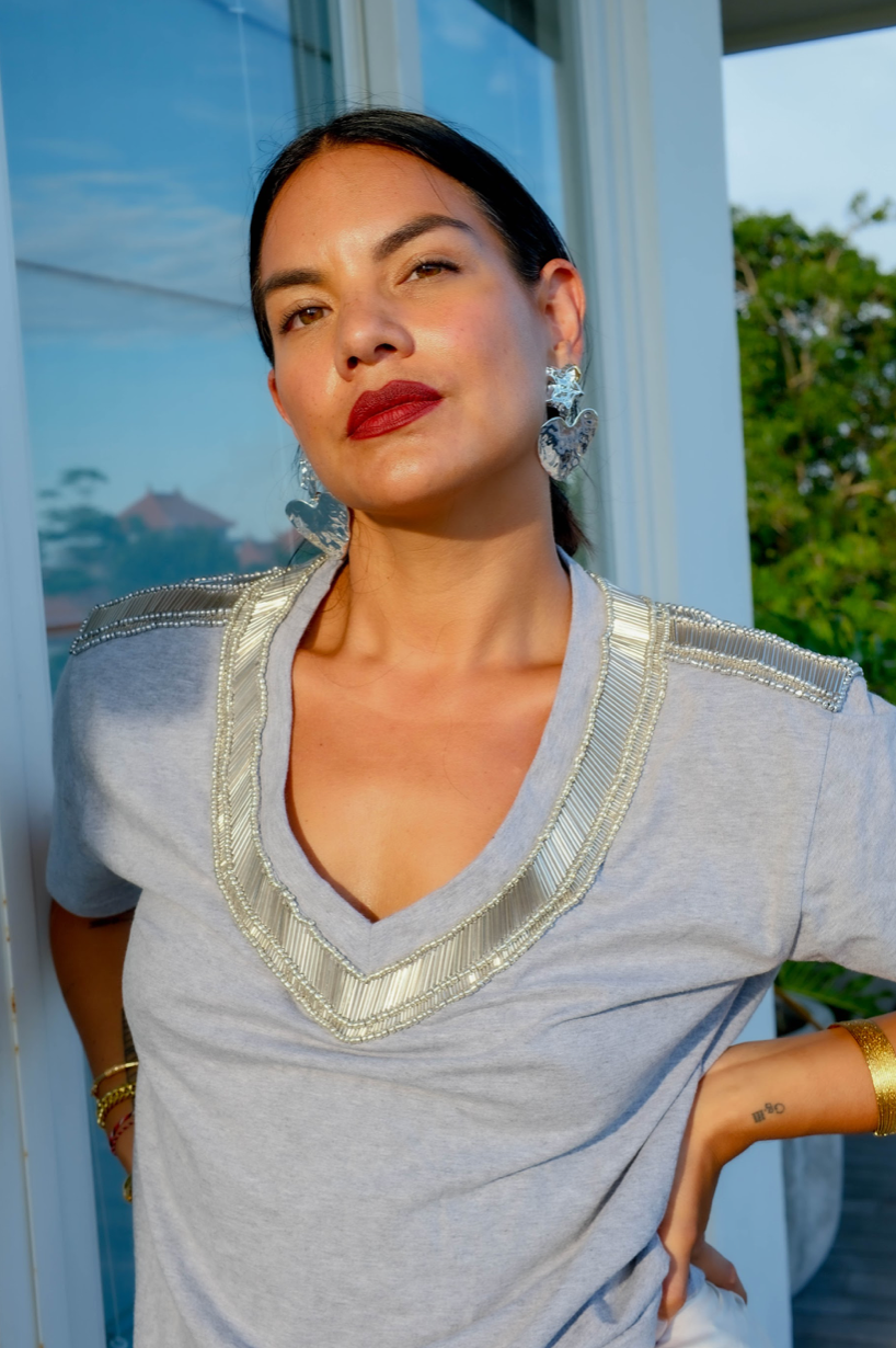 A woman wearing a gray marle t-shirt with a deep V-neck and silver beading across the chest and neck area.